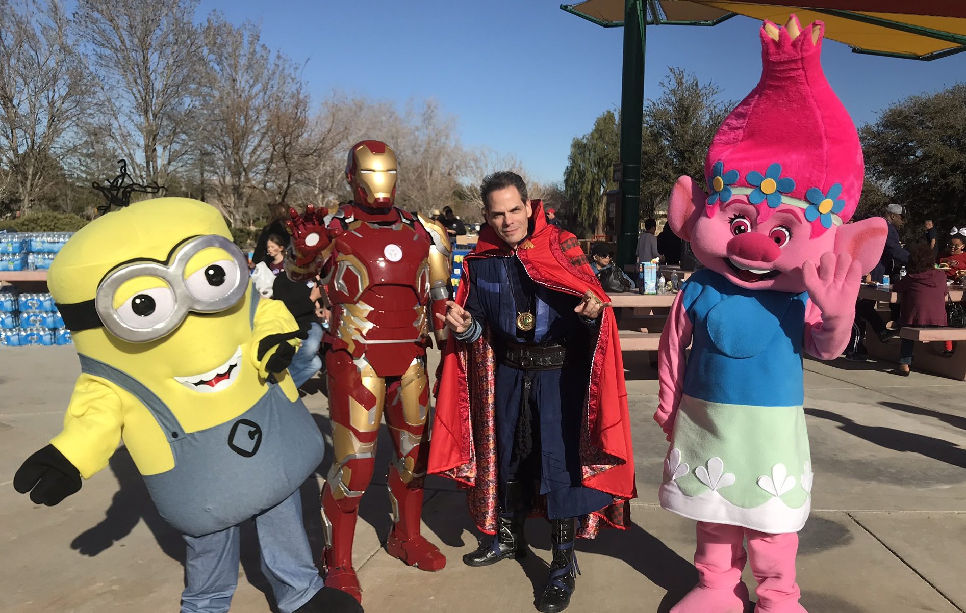 A group of costumed characters, including a Minion, Iron Man, Doctor Strange, and a Trolls character, pose for a photo in an outdoor Las Vegas park setting, symbolizing unexpected events and the need for personal injury protection.