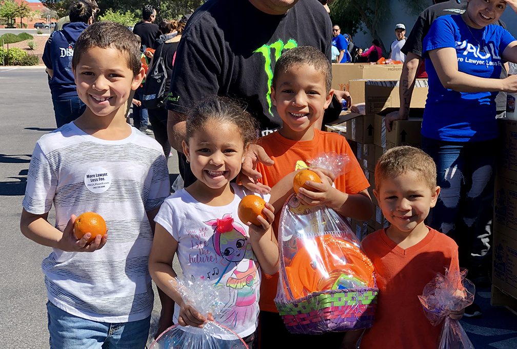 A group of smiling children hold oranges and Easter baskets at a community event hosted by a Las Vegas personal injury law firm, showcasing their commitment to giving back and supporting the local community.