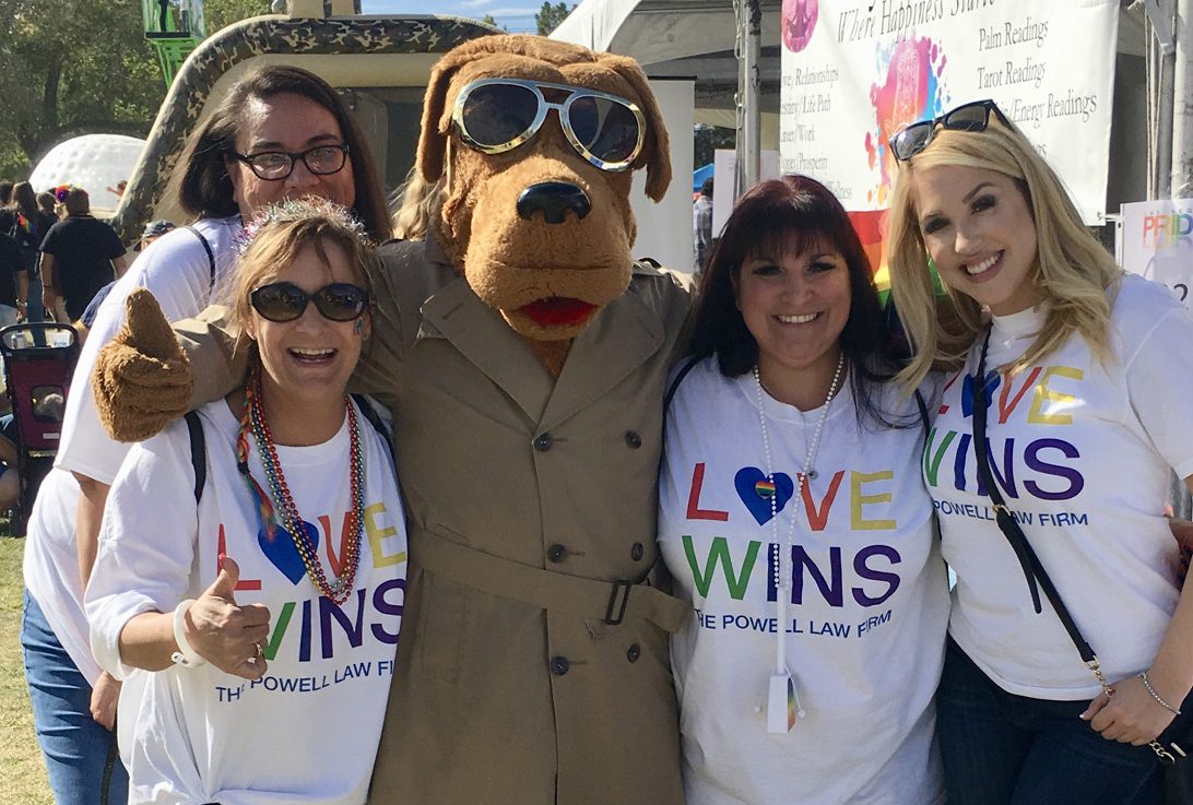 Group photo of smiling women and a dog mascot wearing "Love Wins" shirts for The Powell Law Firm, showcasing their support for the LGBTQ+ community and their Las Vegas legal services, including personal injury law.