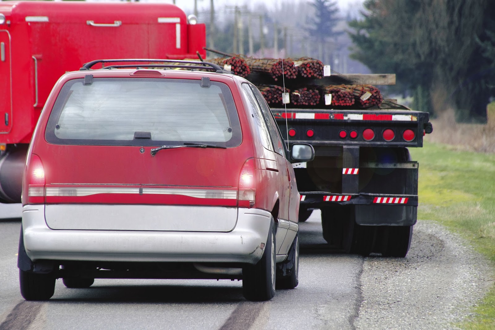 A red minivan is closely following a large truck carrying a load, illustrating the potential danger and risk of personal injury in a truck accident.