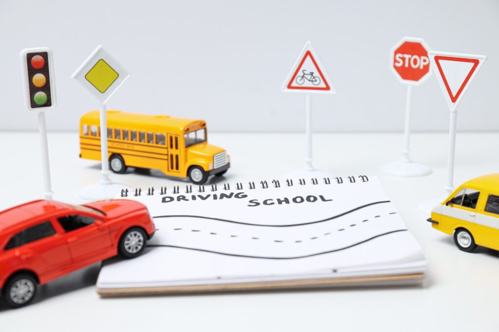 Miniature scene with toy cars, a school bus, road signs, and a notebook that says "Driving School", representing car accidents, traffic safety, personal injury, and legal consultation services in Las Vegas.