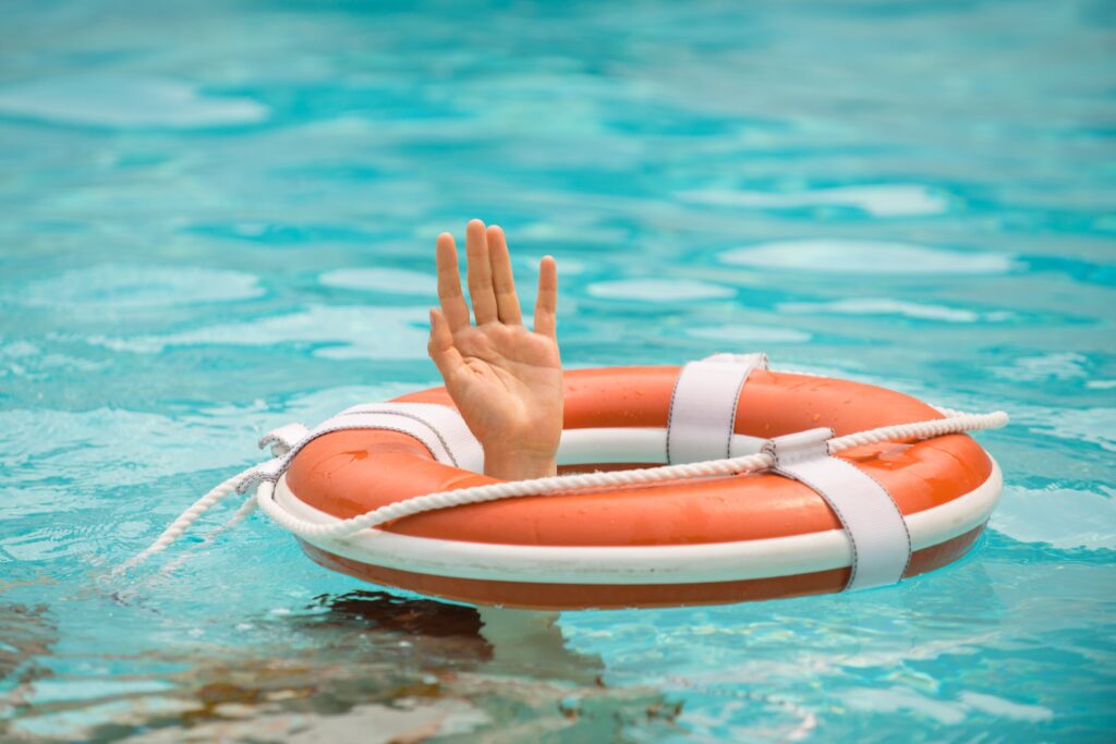 A hand reaches up from the blue water, grasping an orange life preserver, symbolizing a person in need of legal assistance for a swimming pool accident or drowning-related personal injury claim in Las Vegas.