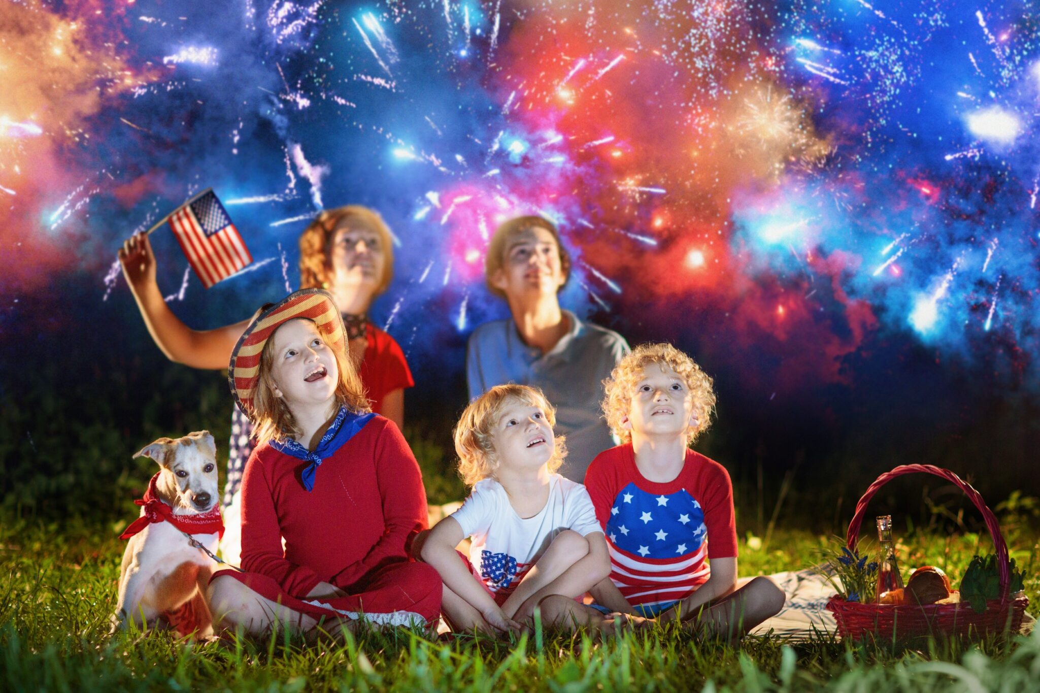 A diverse group of people and a dog joyfully watch fireworks on the Fourth of July, promoting fireworks safety and highlighting personal injury prevention tips for families in Las Vegas to ensure celebrations remain safe.