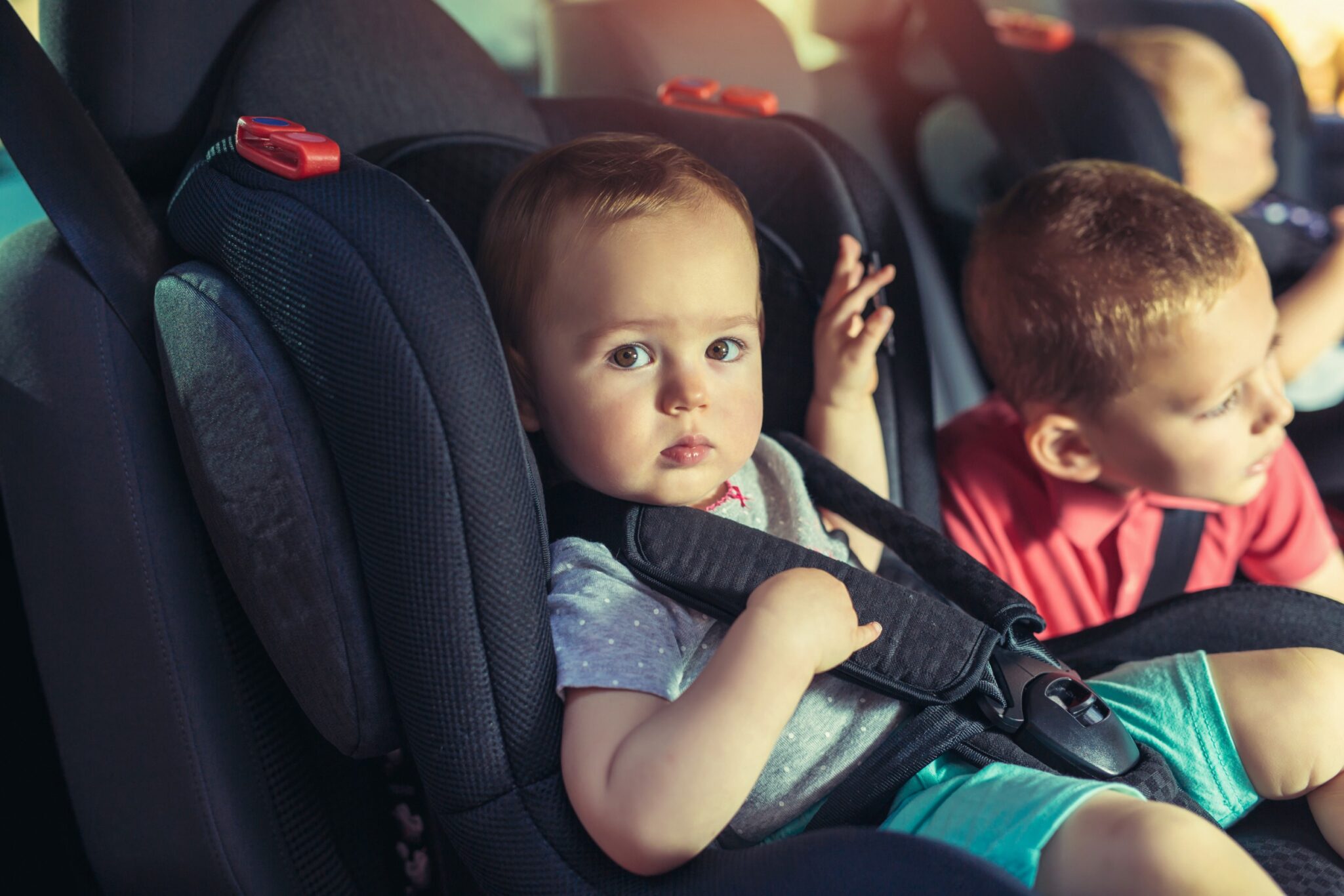 A close-up of two children, a baby and a young boy, buckled into car seats in the backseat of a vehicle, conveying a message of safety and the potential need for legal assistance related to car accidents and personal injury in Las Vegas.