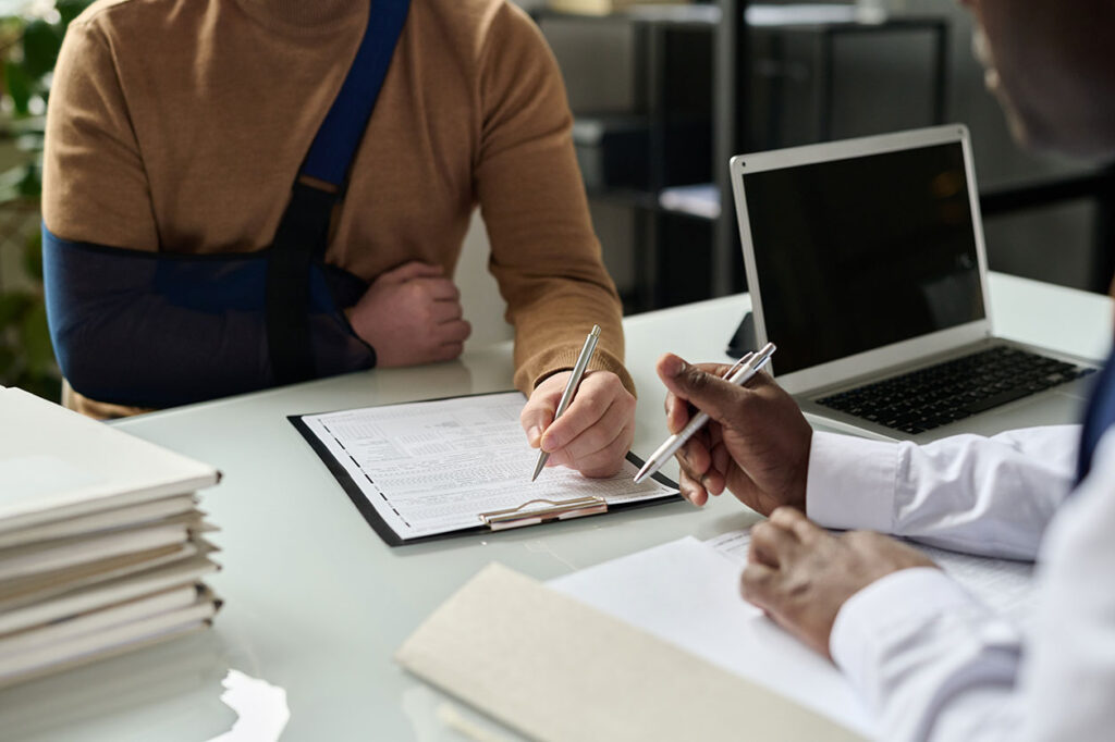 A man with a sling signs paperwork with assistance from a legal professional for a Las Vegas personal injury claim.