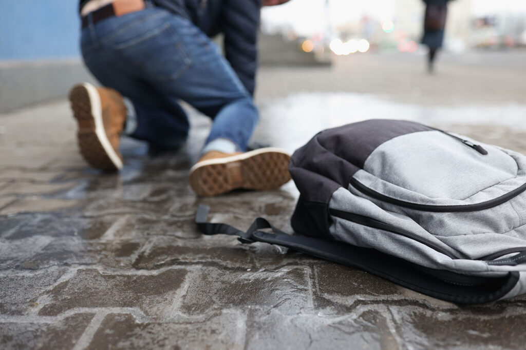 A man is kneeling on a wet pavement after a slip and fall accident, with a backpack nearby, suggesting a potential personal injury claim in Las Vegas.