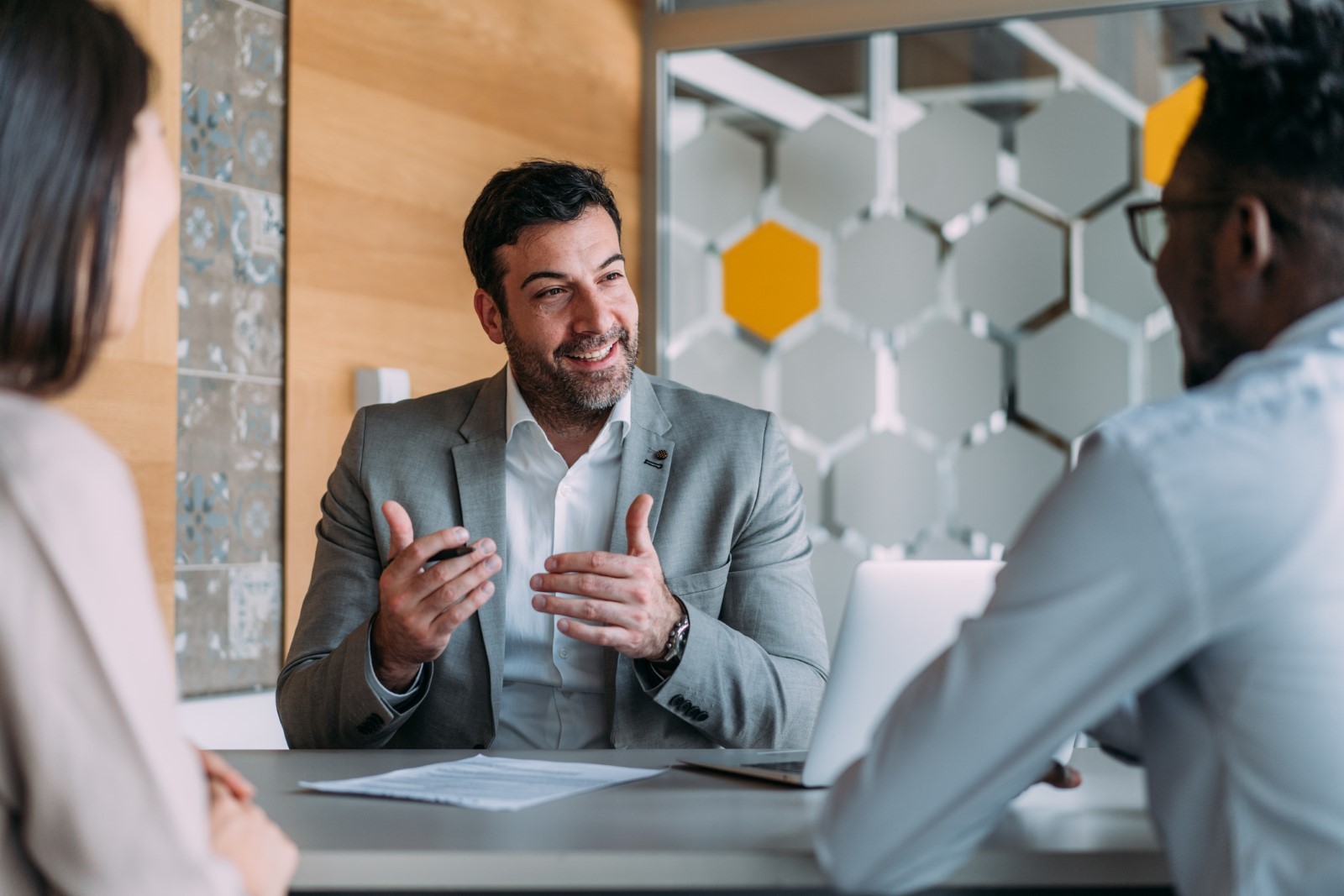 Smiling lawyer in a suit discussing a personal injury case with two clients at a modern Las Vegas law firm office.